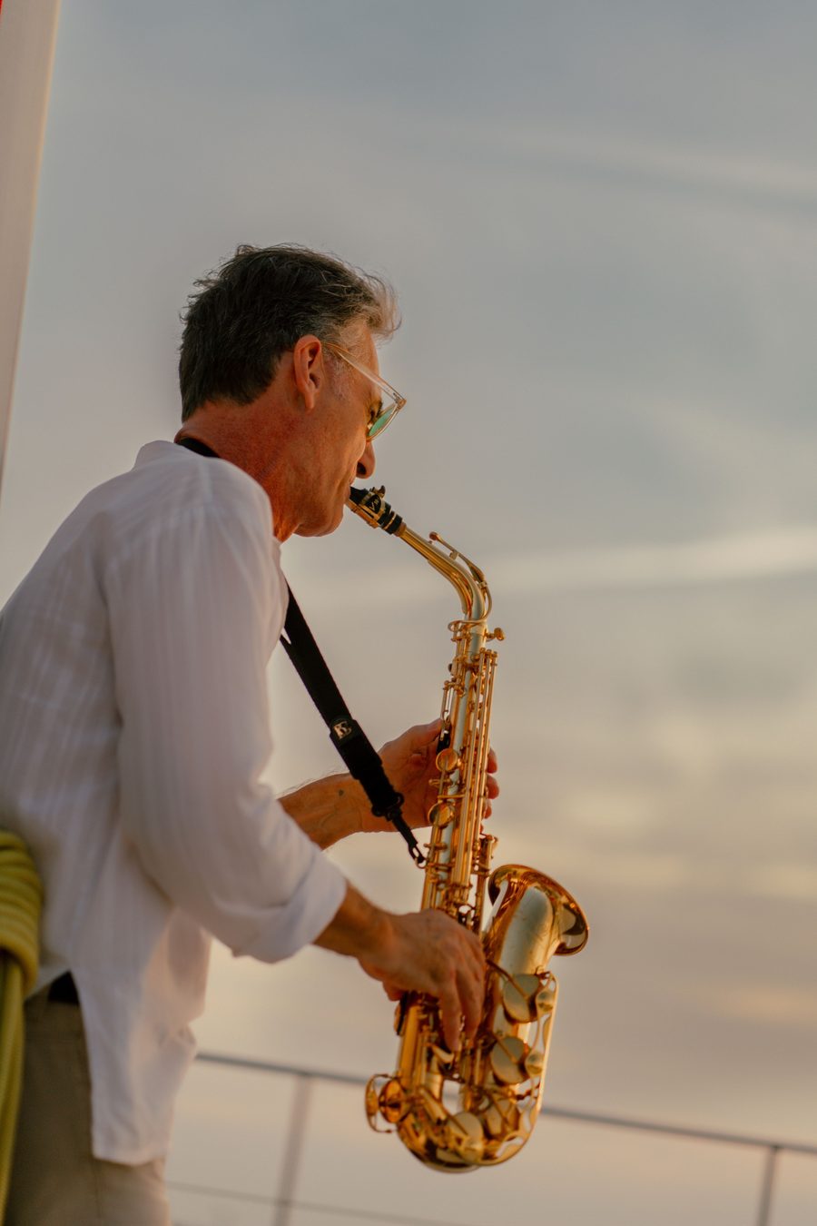 Saxofonist im weißen Hemd spielt bei tiefstehender Sonne über dem Meer, Sunset Session auf Mallorca