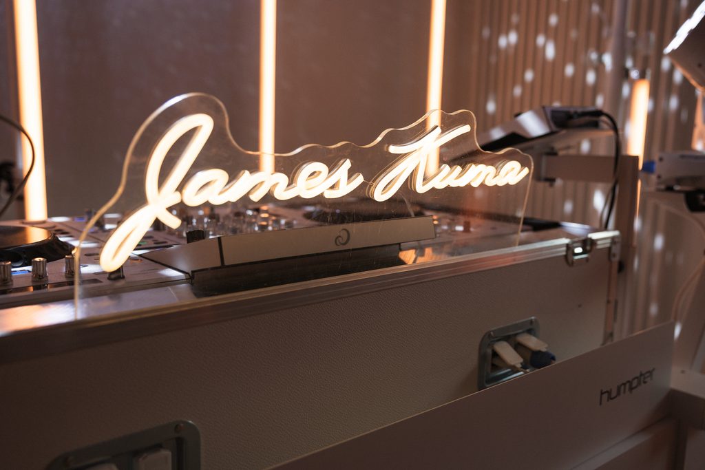 Leuchtender Neon-Schriftzug James Kuma auf der weißen DJ-Booth