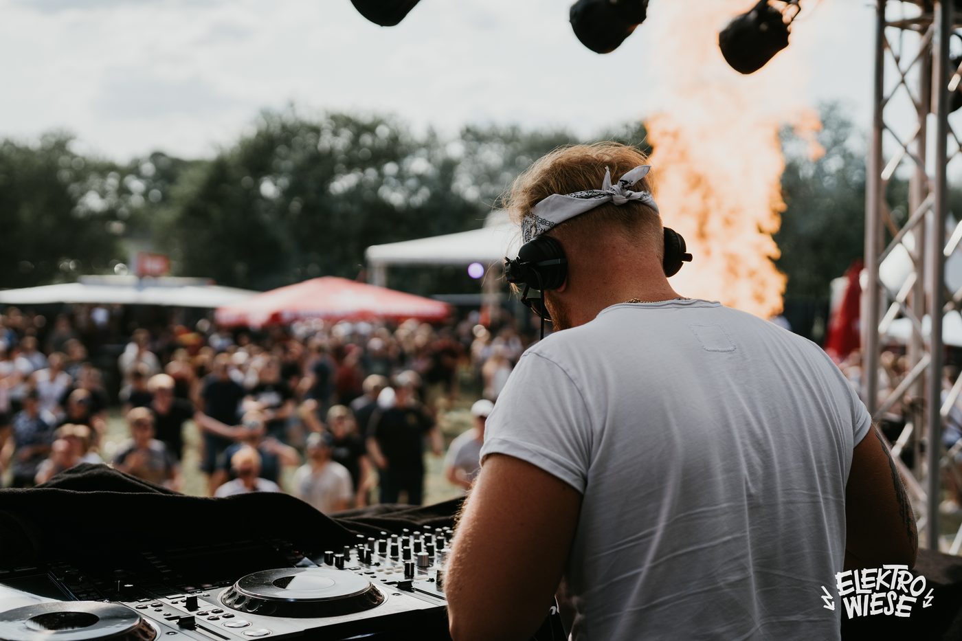 James Kuma von hinten an den Decks auf einer Festivalbühne, vor ihm die Menge, daneben eine Pyro-Flamme