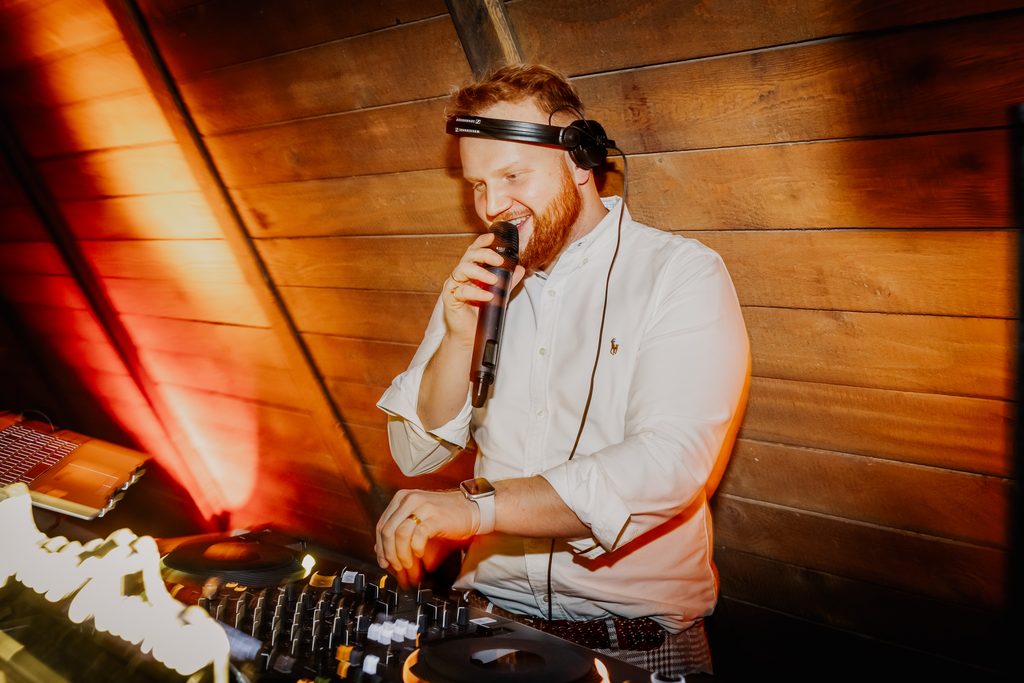 James Kuma am Mikrofon hinter den Decks, warmes Licht
